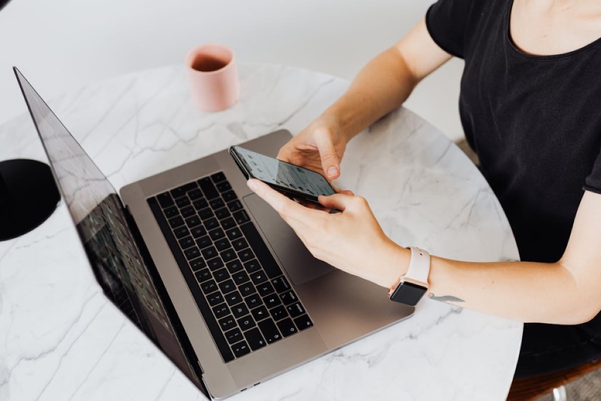 Person setting up maintenance reminders on a smartphone with laptop and smartwatch nearby